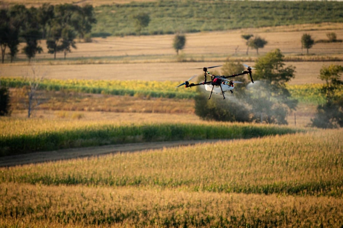 An XAG spray drone working a patchwork of row-crop fields at golden hour